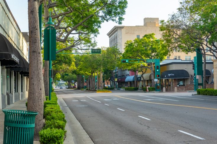 Tree-lined Downtown Fullerton street along Harbor Boulevard with storefronts and a quiet morning roadway