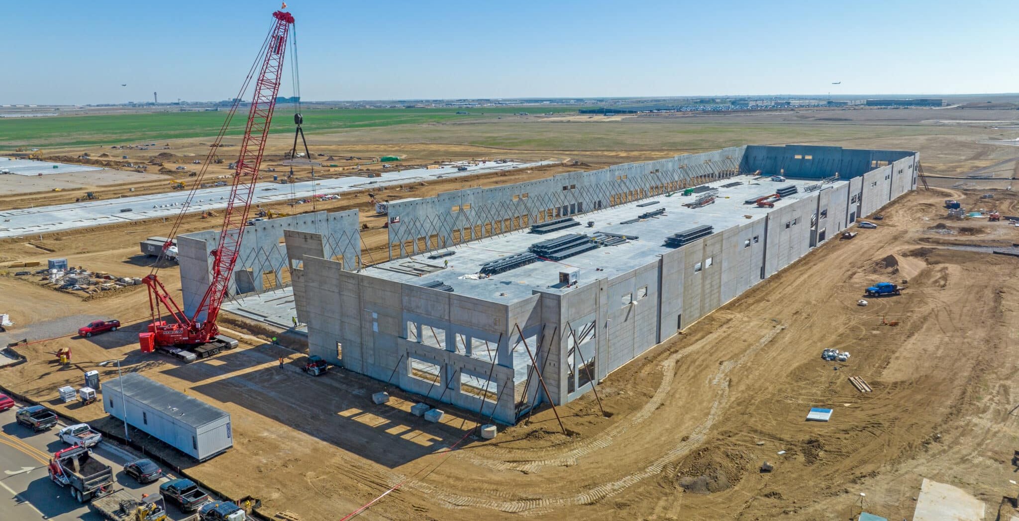 Tilt-up concrete distribution warehouse under construction with a crane on a dirt Inland Empire pad