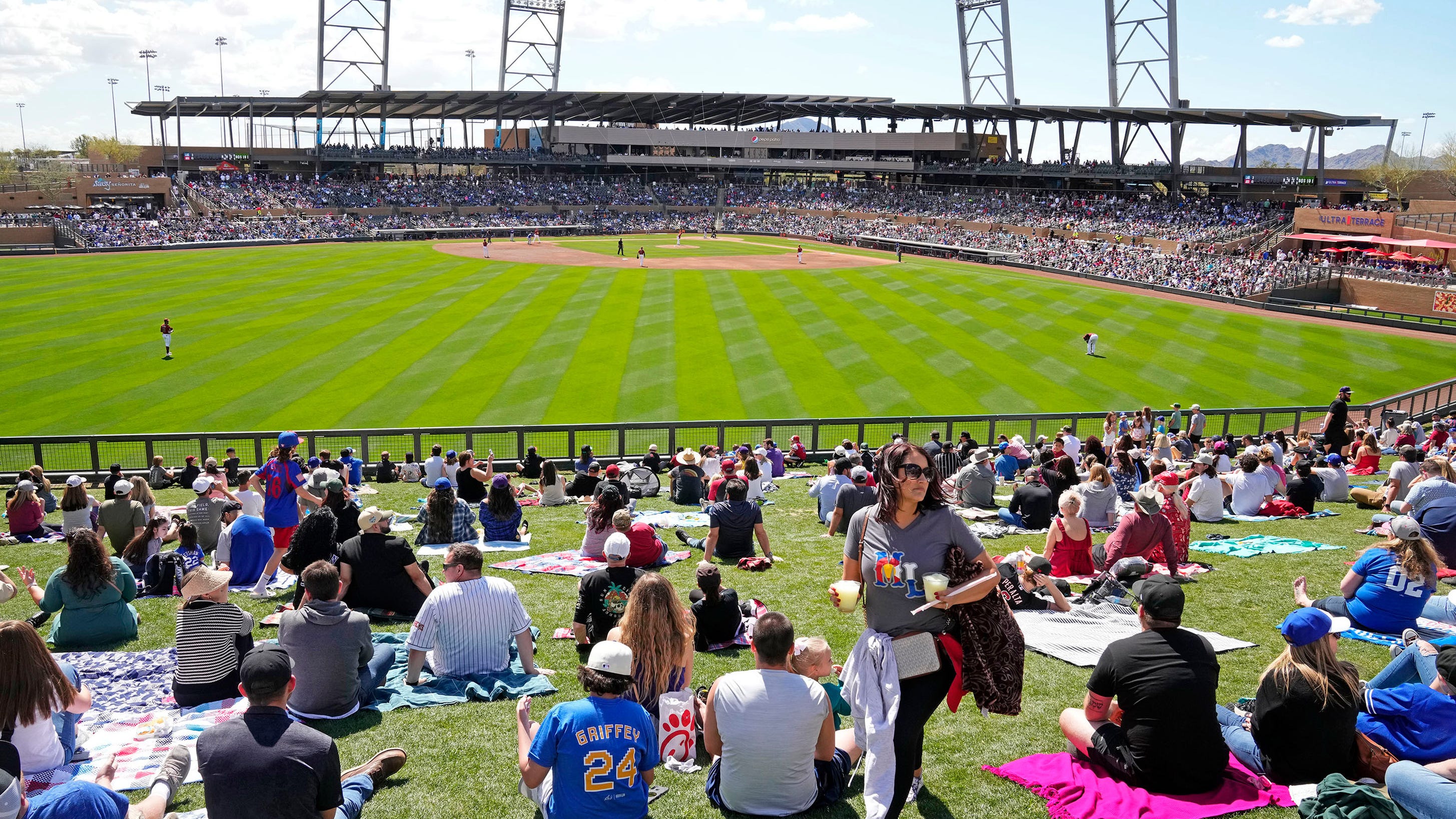 Large outdoor crowd on the berm at a Mesa spring-training ballpark on a sunny Cactus League afternoon