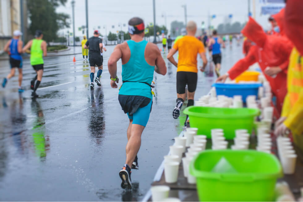 Runners passing an outdoor aid station with cups and coolers during a Salt Lake Valley road race