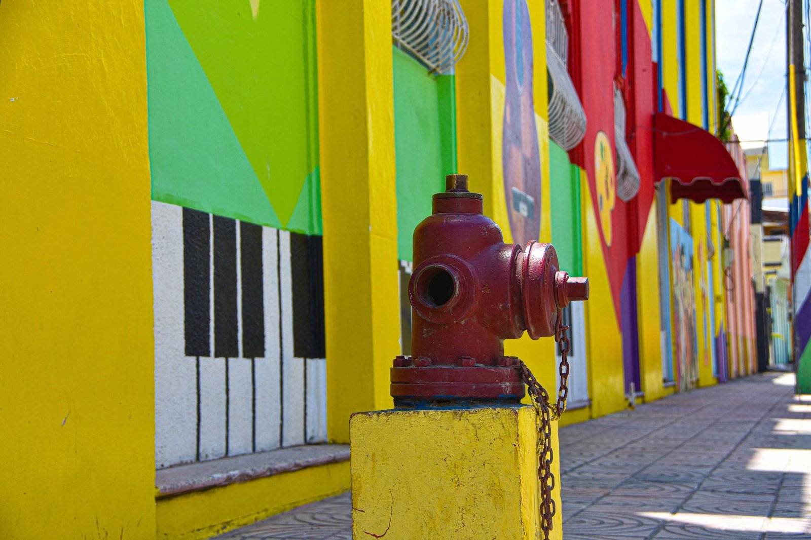 A colorful mural-painted building with piano-key artwork and a red fire hydrant on the sidewalk