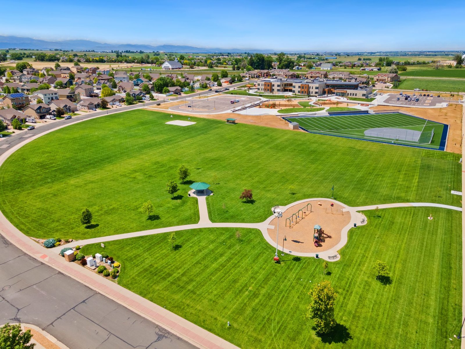 An aerial view of a community sports field and playground with mountains in the distance