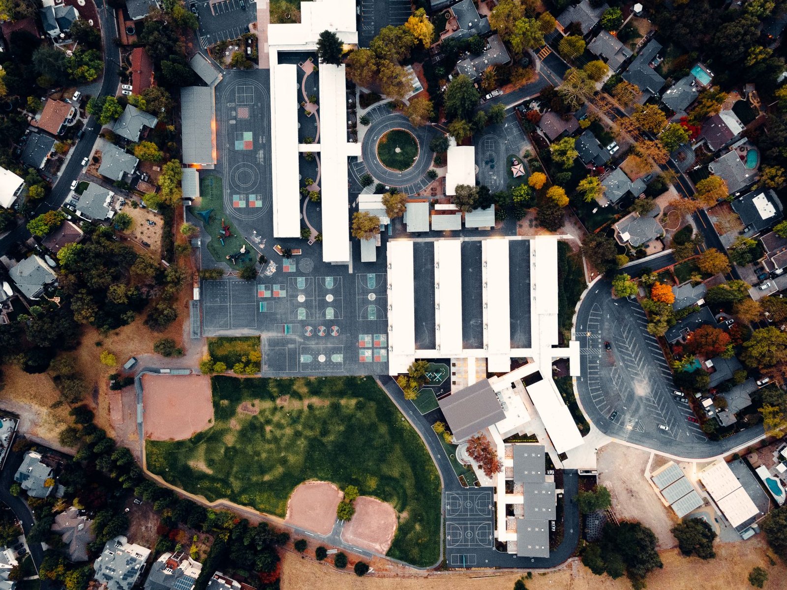 An aerial view of a school campus with basketball courts and a playground in a residential neighborhood