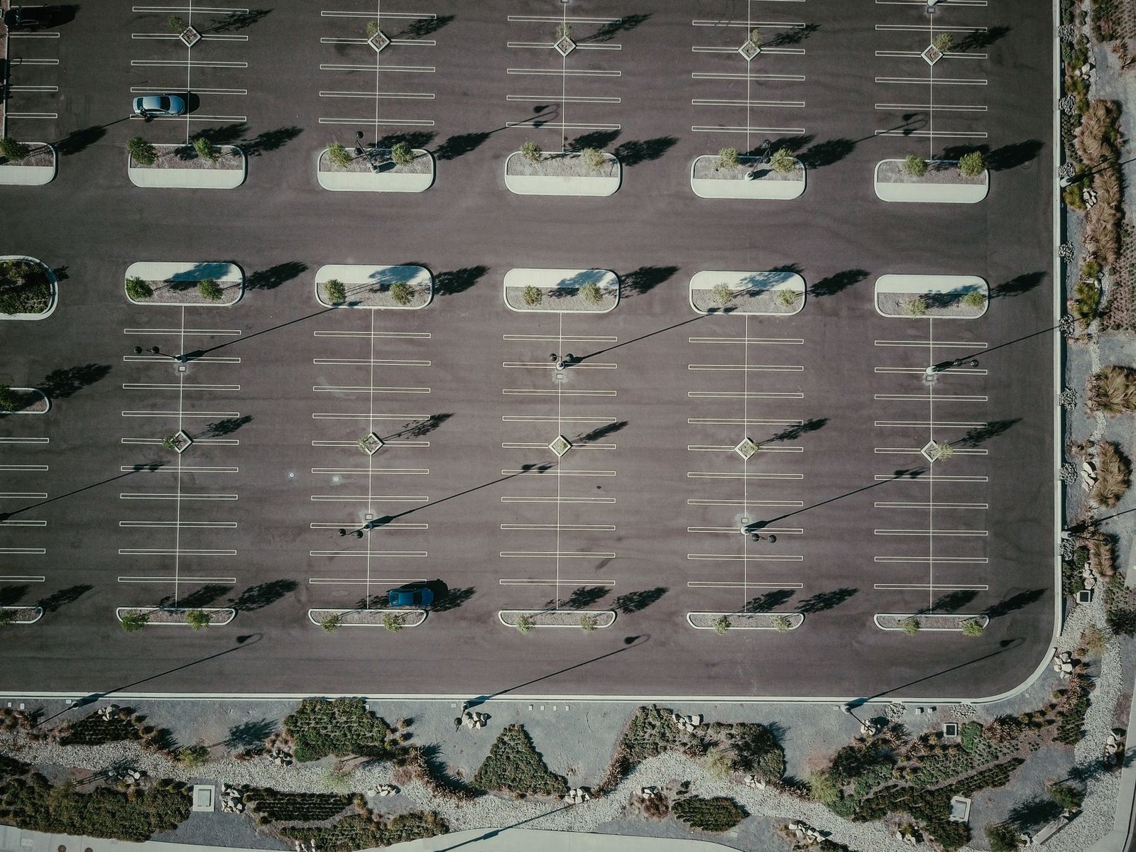 An aerial view of a nearly empty asphalt parking lot with drought-tolerant landscaping