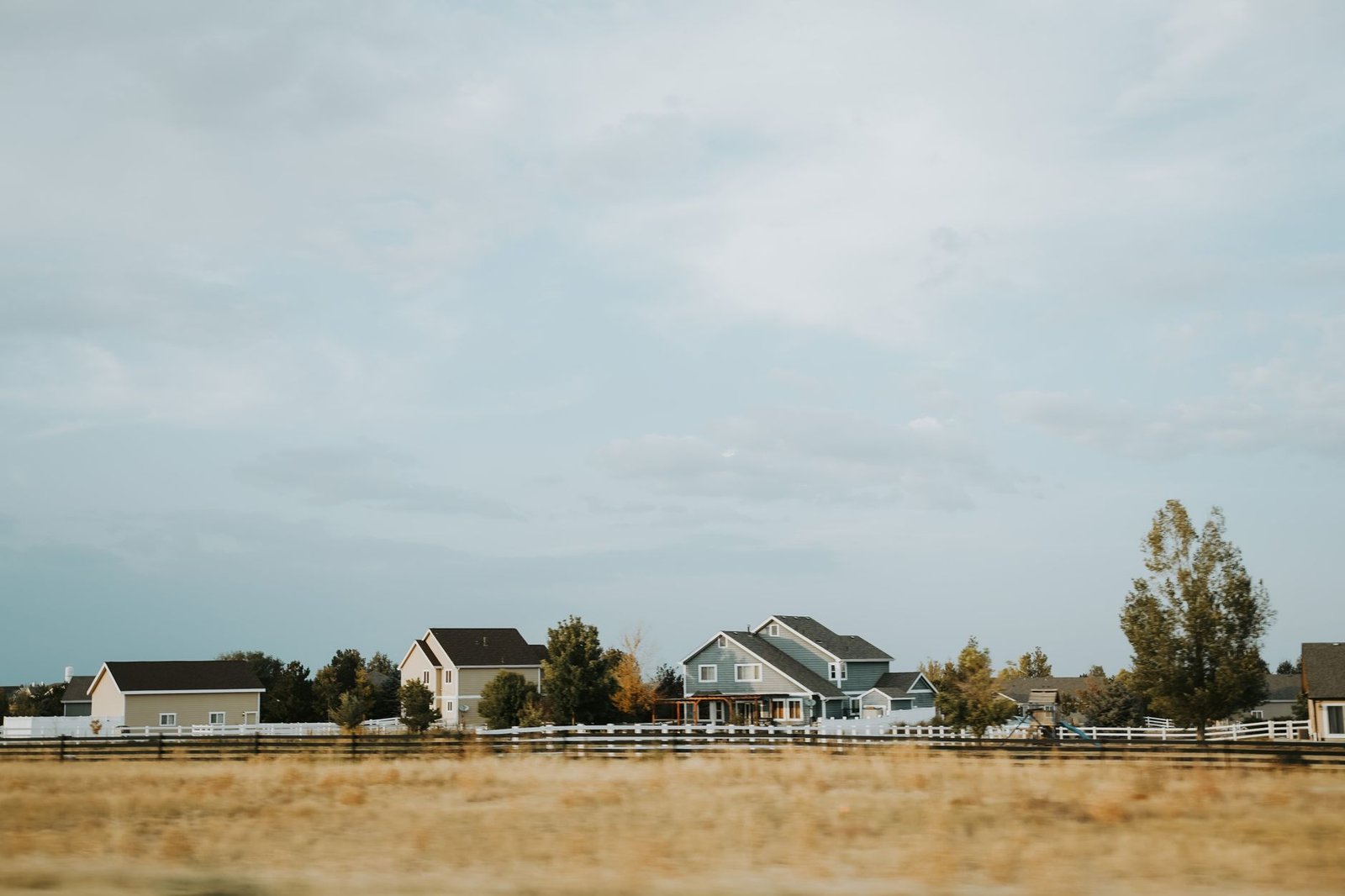 Houses behind a white fence in a Colorado subdivision with open prairie in front
