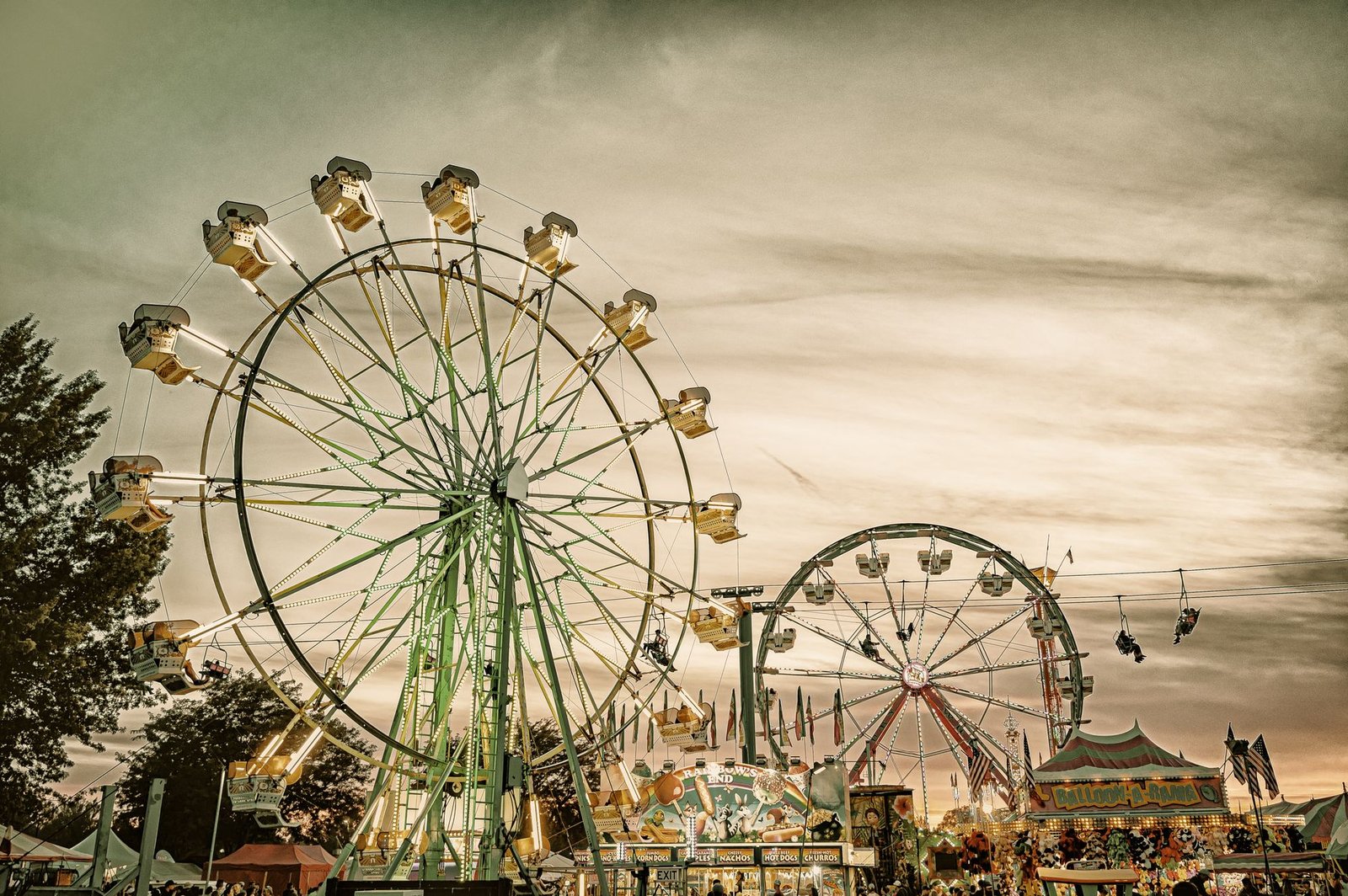 Carnival Ferris wheels lit up at dusk at a fairgrounds midway