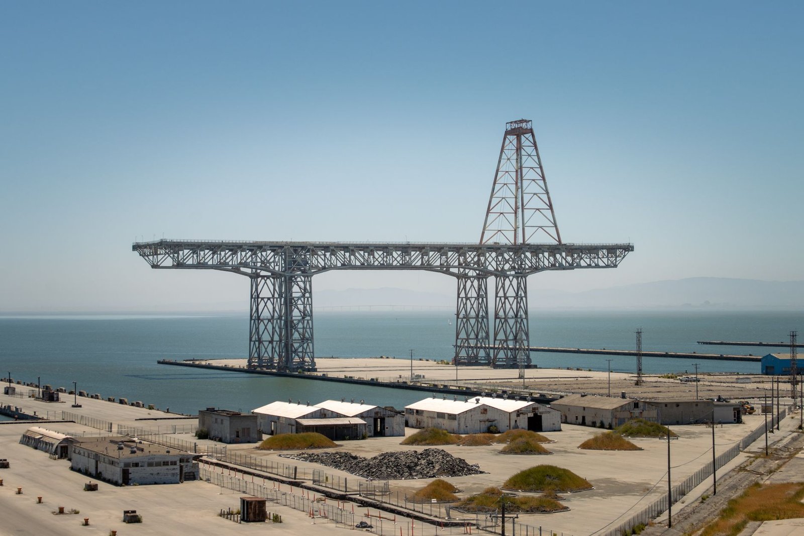 A tall steel shipyard gantry crane over an empty dry dock beside waterfront warehouses