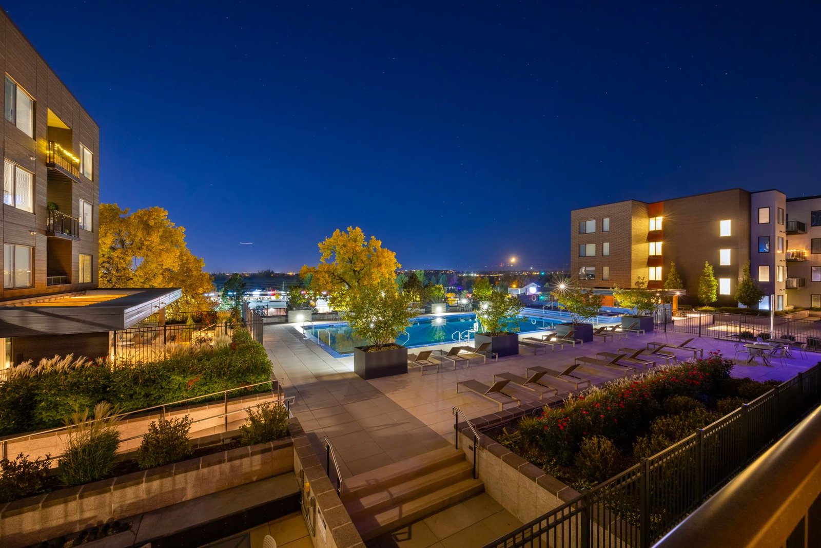 Newer apartment buildings and a lit courtyard pool at dusk in a Colorado suburb