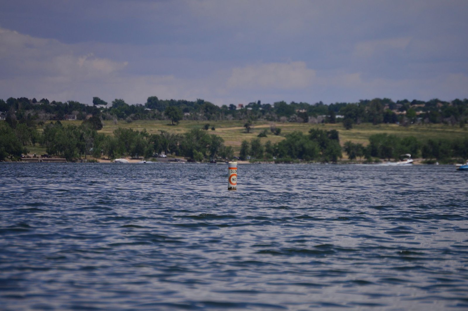 Open water and a no-wake buoy on a Front Range reservoir with a tree-lined shore